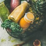 Colorful smoothies in bottles with fruits in basket, grey background
